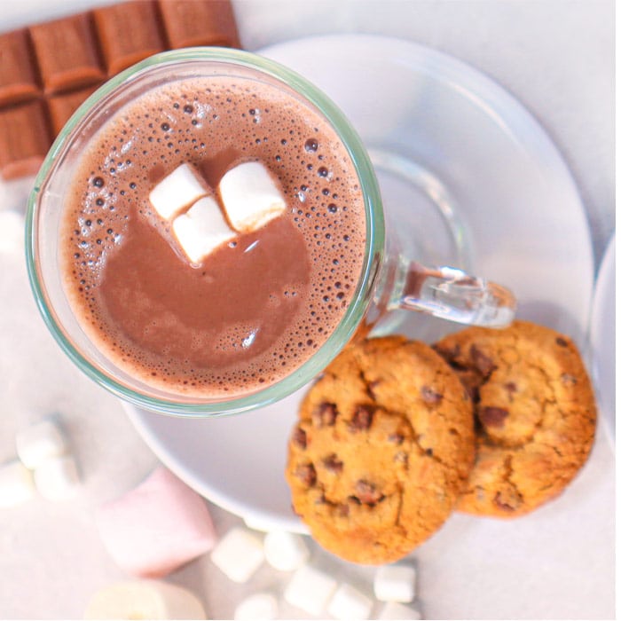 hot-chocolate-recipe-02 A glass of hot chocolate topped with marshmallows, accompanied by chocolate chip cookies.