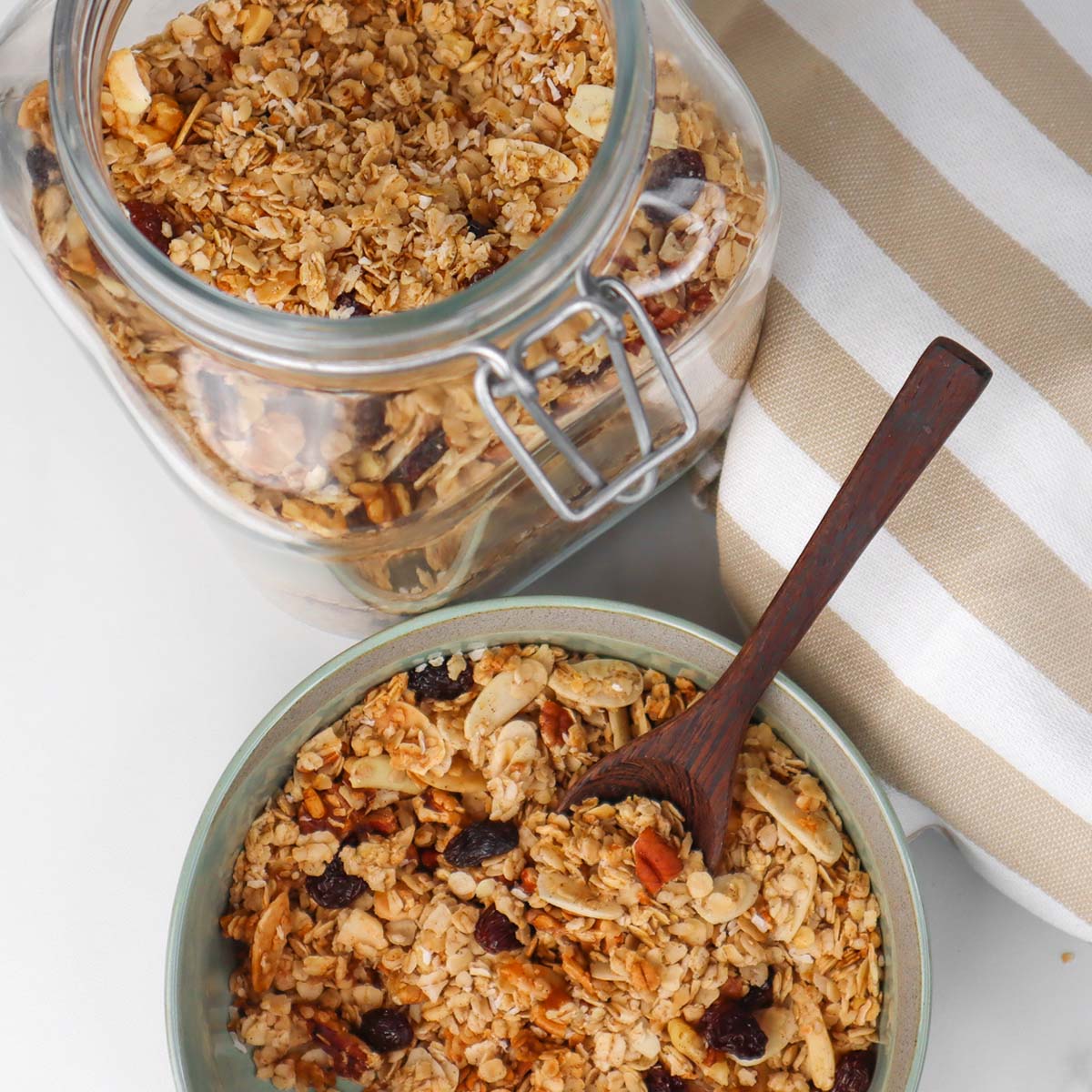 Muesli Een kom granola met noten en gedroogd fruit, een pot granola en een houten lepel.