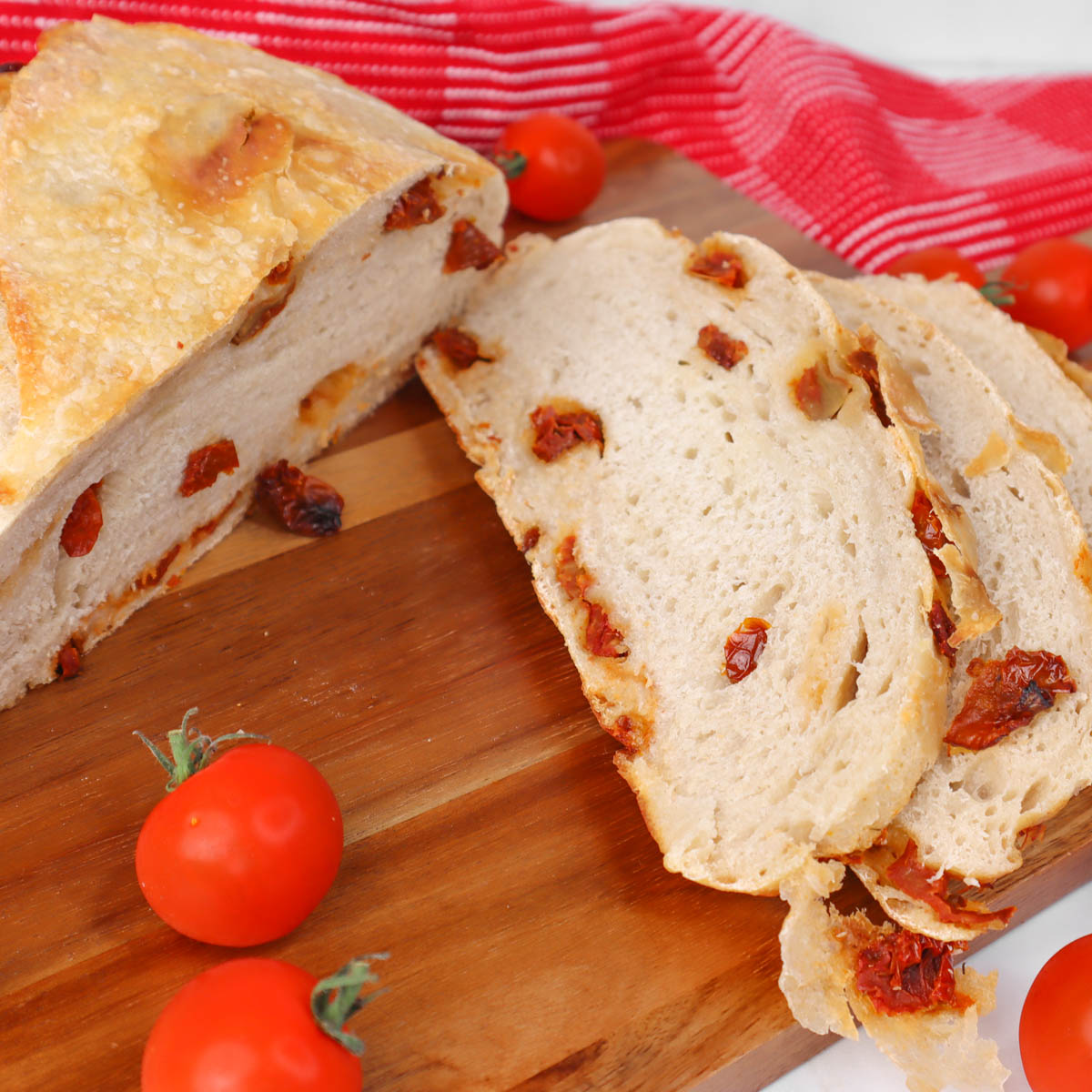 Sundried tomato Sourdough Bread Sliced sourdough bread with sundried tomatoes on a wooden board, accompanied by cherry tomatoes.