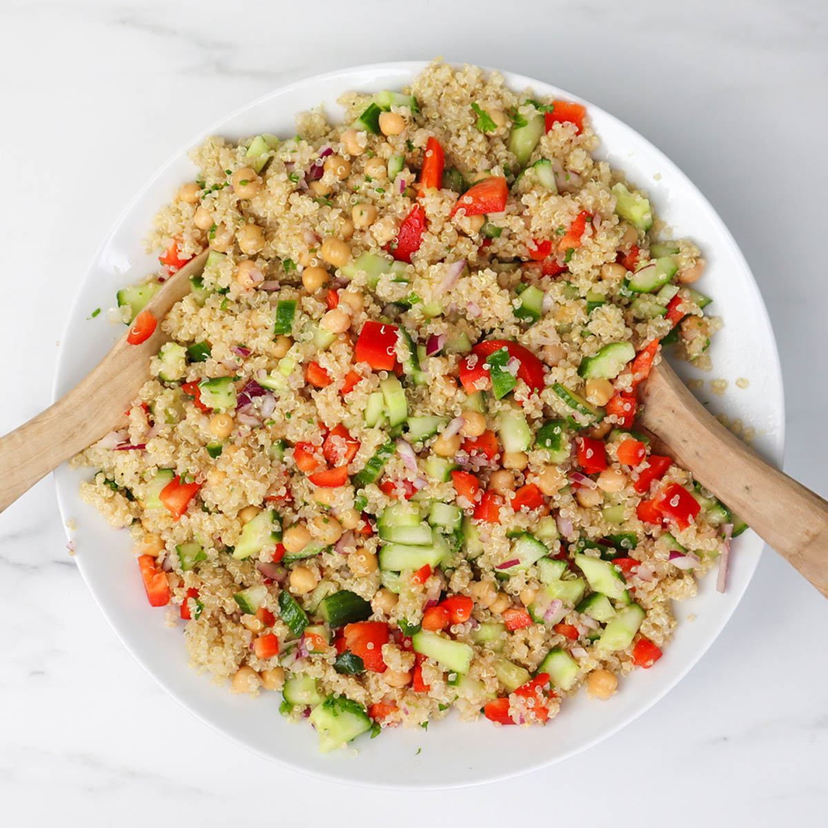 Salade de quinoa Une salade de quinoa colorée avec des pois chiches, des concombres et des poivrons dans un bol blanc.