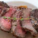 Irisan daging sapi matang dengan sedikit warna merah muda dan dihiasi dengan setangkai timi.