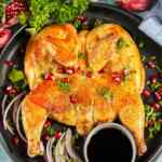 Ayam yang dimasak dengan indah, diberi taburan rempah-rempah dan biji delima, disajikan di atas piring hitam.