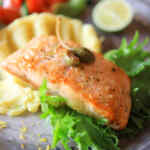 Fillet salmon matang disajikan di atas hamparan selada dengan kentang tumbuk dan irisan jeruk nipis.