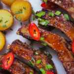 Iga matang yang dihias dengan daun bawang dan irisan cabai merah, disajikan dengan kentang panggang keemasan.