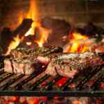 Steak panggang dengan bumbu di atas panggangan barbekyu di atas bara api.