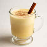 Segelas eggnog dengan taburan kayu manis dan pala di atasnya.