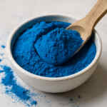 Semangkuk bubuk spirulina biru cerah dengan sendok kayu.