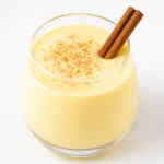Segelas eggnog dengan taburan kayu manis dan pala di atasnya.