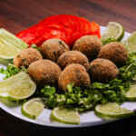 Falafels en un plato para servir rodeados de lechuga, tomates y rodajas de lima.