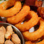 Aros de cebolla crujientes en un plato con un pequeño tazón de nueces