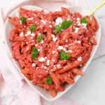 Un tazón en forma de corazón de pasta de hummus de remolacha cubierto con perejil y queso desmenuzado.