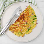 Tortilla de queso y hierbas adornada con cebollino, servida en un plato con tenedor y cuchillo.