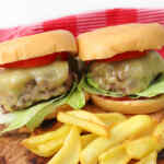 Dos hamburguesas caseras de carne con queso, lechuga y tomate, servidas con papas fritas doradas.