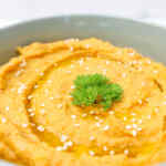 Un tazón de hummus marroquí cubierto con semillas de sésamo y una ramita de perejil.