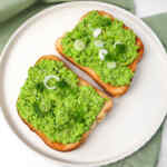 Dos rebanadas de pan tostado cubiertas con guisantes machacados, cebollas verdes y semillas de sésamo.