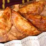 Pastel khas Cornwall berwarna coklat keemasan disusun di atas papan kayu, dengan peta perkamen di bawahnya.