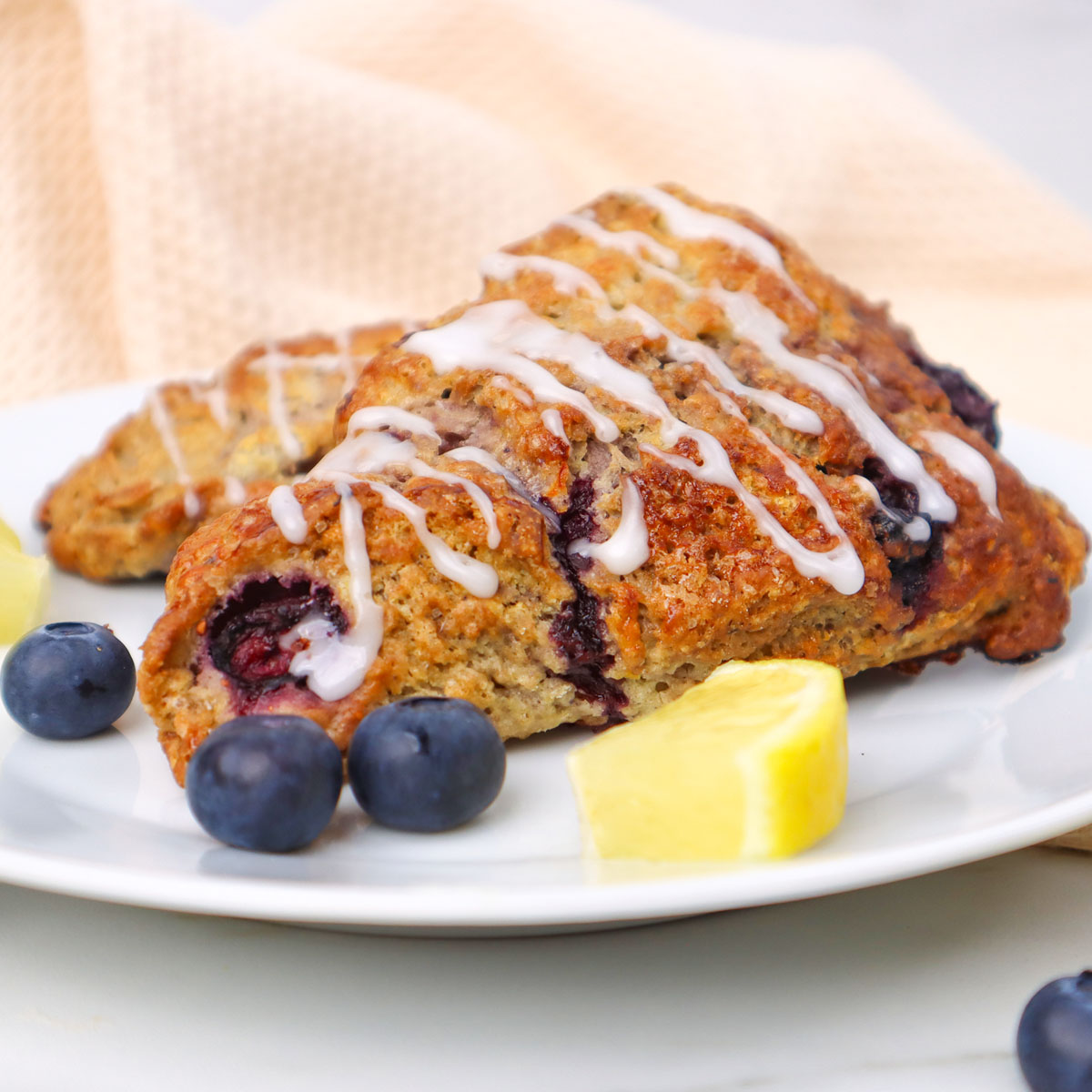 Frisch gebackene Blaubeer-Scones mit Zuckerguss beträufelt, serviert mit Blaubeeren und Zitronenspalten.