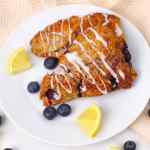 Dua scone blueberry yang dilumuri lapisan gula, diberi potongan lemon dan blueberry segar.