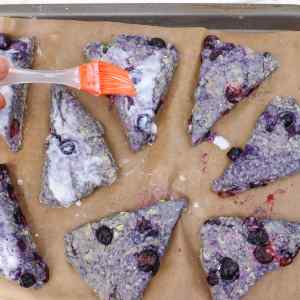 Frisch gebackene Blaubeer-Scones werden auf einem Backblech mit Glasur bestrichen.