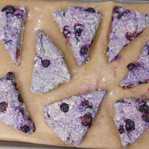 Frisch gebackene Blaubeer-Scones auf Backpapier, die ihre violette Farbe und die verstreuten Blaubeeren zur Geltung bringen.