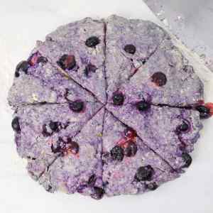 Ein runder, ungebackener Blaubeer-Scone-Teig, der auf einer bemehlten Oberfläche in Keile geschnitten wird.
