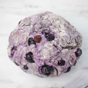 Eine Kugel aus Blaubeer-Scone-Teig mit sichtbaren Blaubeeren und einem violetten Farbton.