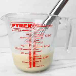 A measuring cup with a whisk, containing buttermilk, egg, and vanilla extract.