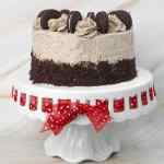 Kue Oreo berlapis-lapis, diberi potongan kue Oreo dan gulungan frosting di atas tatakan kue dekoratif.