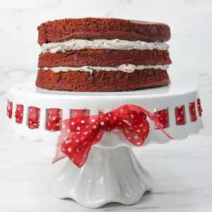 Kue berlapis dengan isi krim Oreo di atas tatakan kue dekoratif, dihiasi pita polkadot merah.