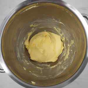 Mangkuk pencampur yang diisi dengan krim mentega berwarna kuning lembut.