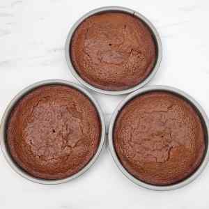 Tiga lapisan kue coklat panggang dalam loyang bundar di atas permukaan marmer.