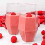 Dua gelas smoothie pisang raspberi dengan tambahan buah raspberi segar.