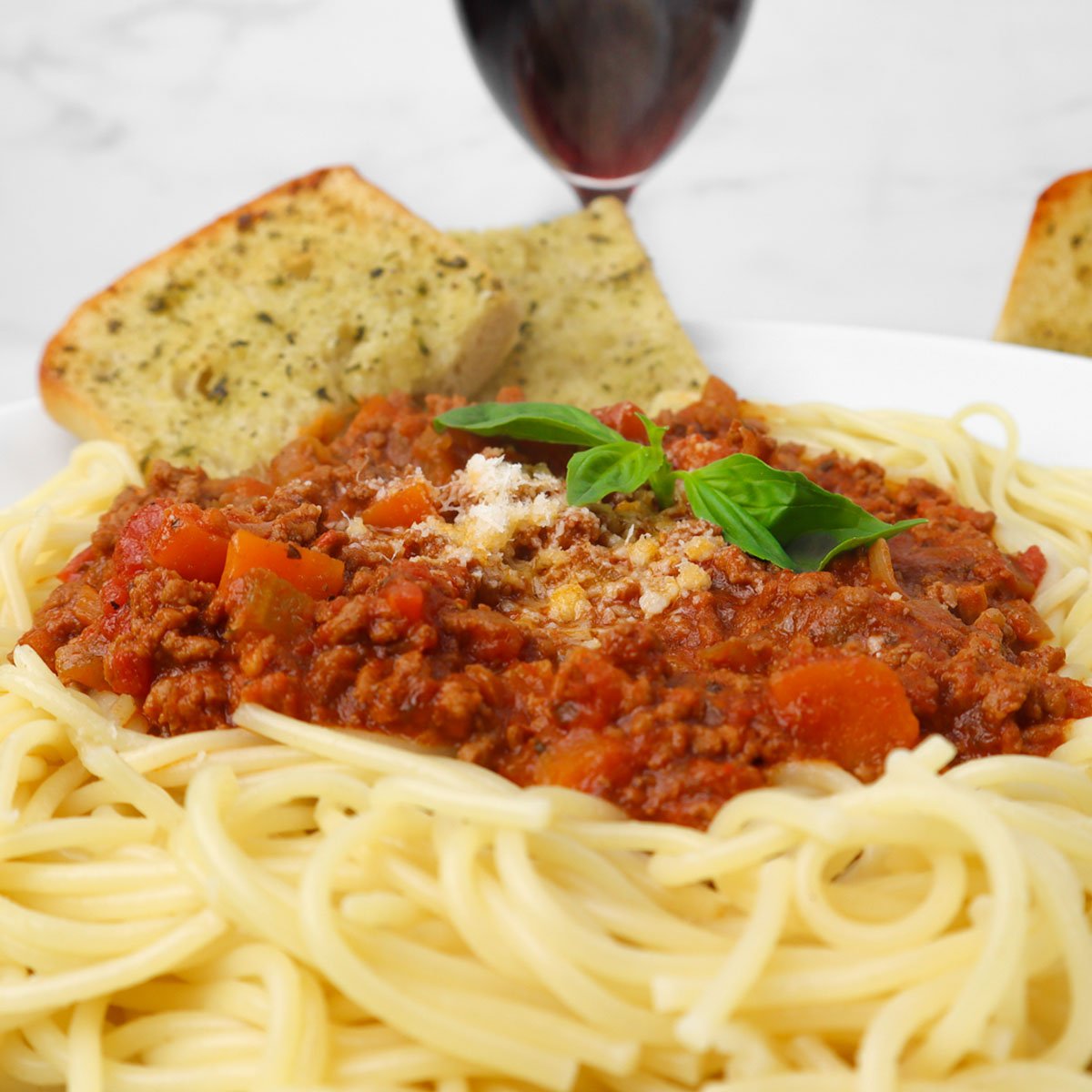 A plate of traditional spaghetti Bolognese topped with basil and served with garlic bread.