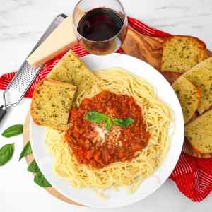 A plate of spaghetti Bolognese topped with basil, served with garlic bread and a glass of red wine.