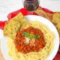 Ein Teller Spaghetti Bolognese mit Basilikum, serviert mit Knoblauchbrot und einem Glas Rotwein.