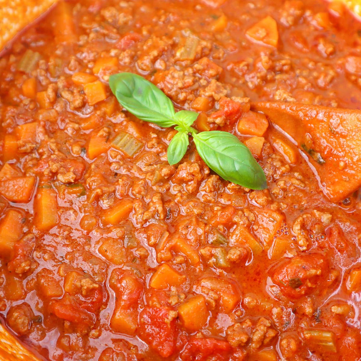 A close-up of a rich spaghetti Bolognese sauce with ground meat and vegetables, garnished with fresh basil.