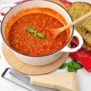 A pot of traditional spaghetti Bolognese with fresh basil and garlic bread on the side.