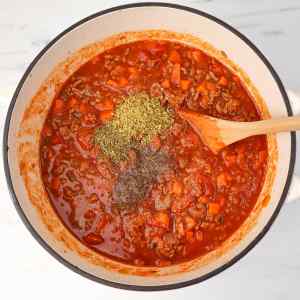 A pot of simmering spaghetti Bolognese sauce with herbs and spices added.