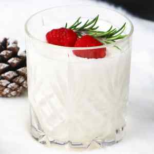 A creamy white cocktail garnished with raspberries and rosemary, set against a soft background.