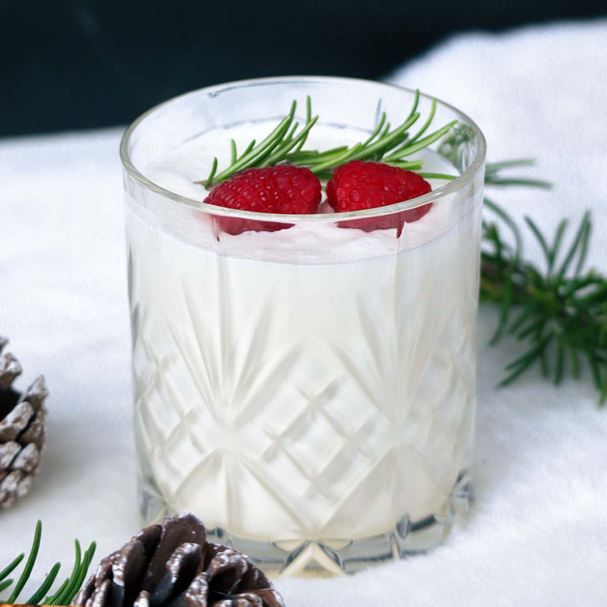 Um coquetel branco festivo decorado com framboesas e alecrim em uma taça de cristal.