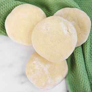 Quatre muffins anglais crus sur une surface en marbre, à côté d'un linge vert.