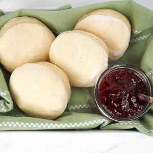 Panecillos ingleses recién hechos en freidora de aire, servidos con un tarro de mermelada sobre un paño verde.