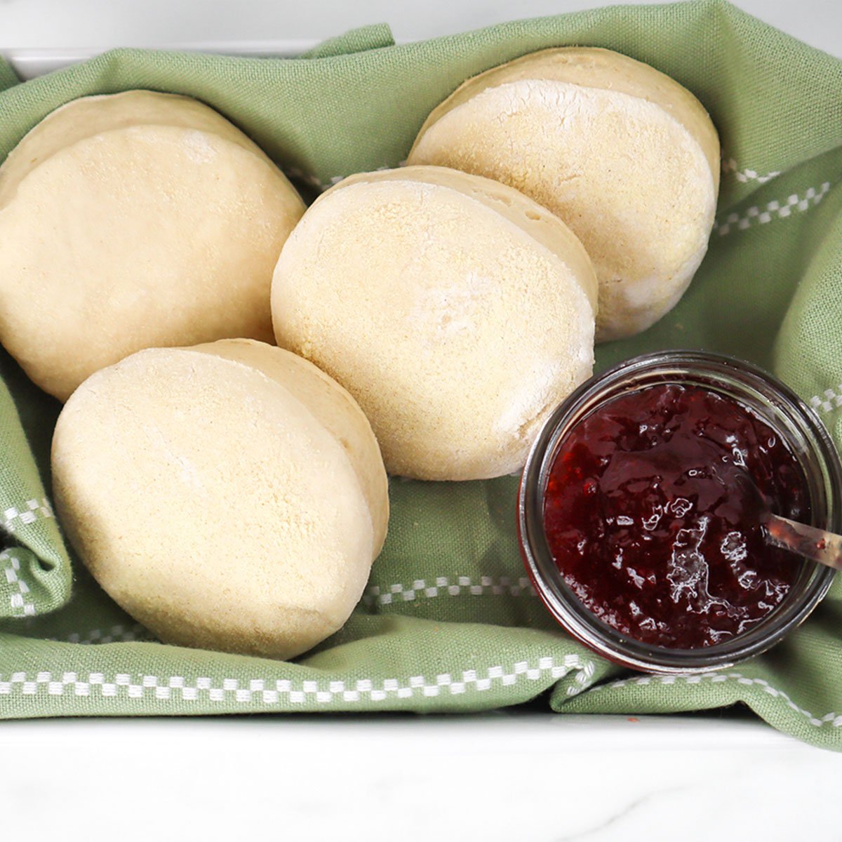 Muffins anglais fraîchement préparés à la friteuse à air, servis avec un pot de confiture sur un linge vert.