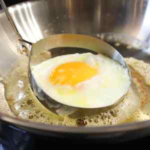 On retire un moule à œuf rond qui entoure un œuf au plat dans une poêle.