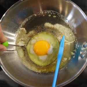 On place un jaune d'œuf dans un moule à œuf rond, lui-même placé dans une poêle contenant du beurre fondu.