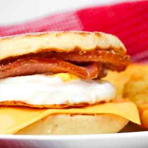 Gros plan sur un muffin maison aux œufs et au bacon, garni de fromage, présenté dans une assiette.