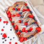 Tostada francesa horneada cubierta con fresas frescas, frambuesas y arándanos, espolvoreada con azúcar en polvo.