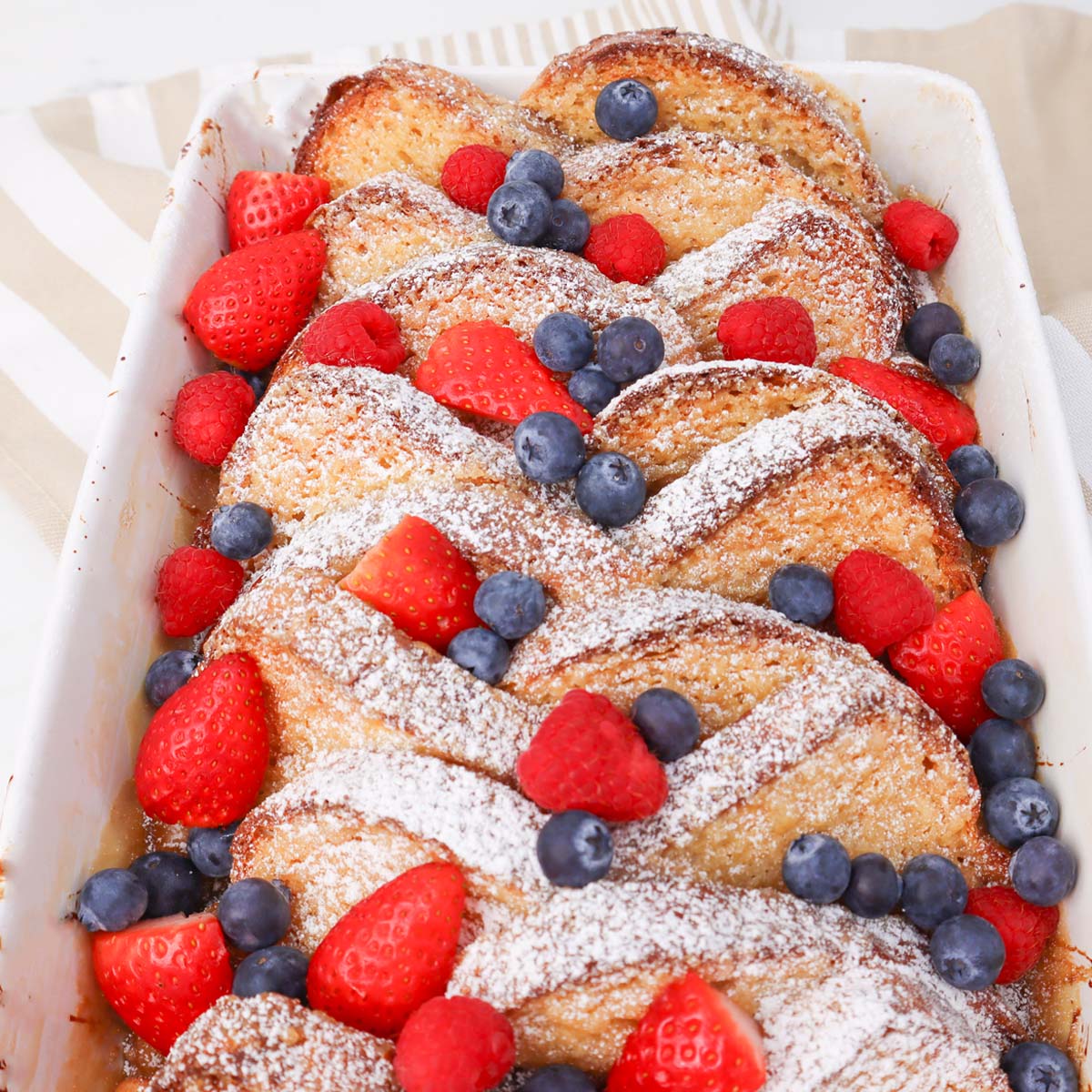 Baked French Toast with Caramel Sauce Baked French toast topped with strawberries, raspberries, and blueberries, dusted with powdered sugar.