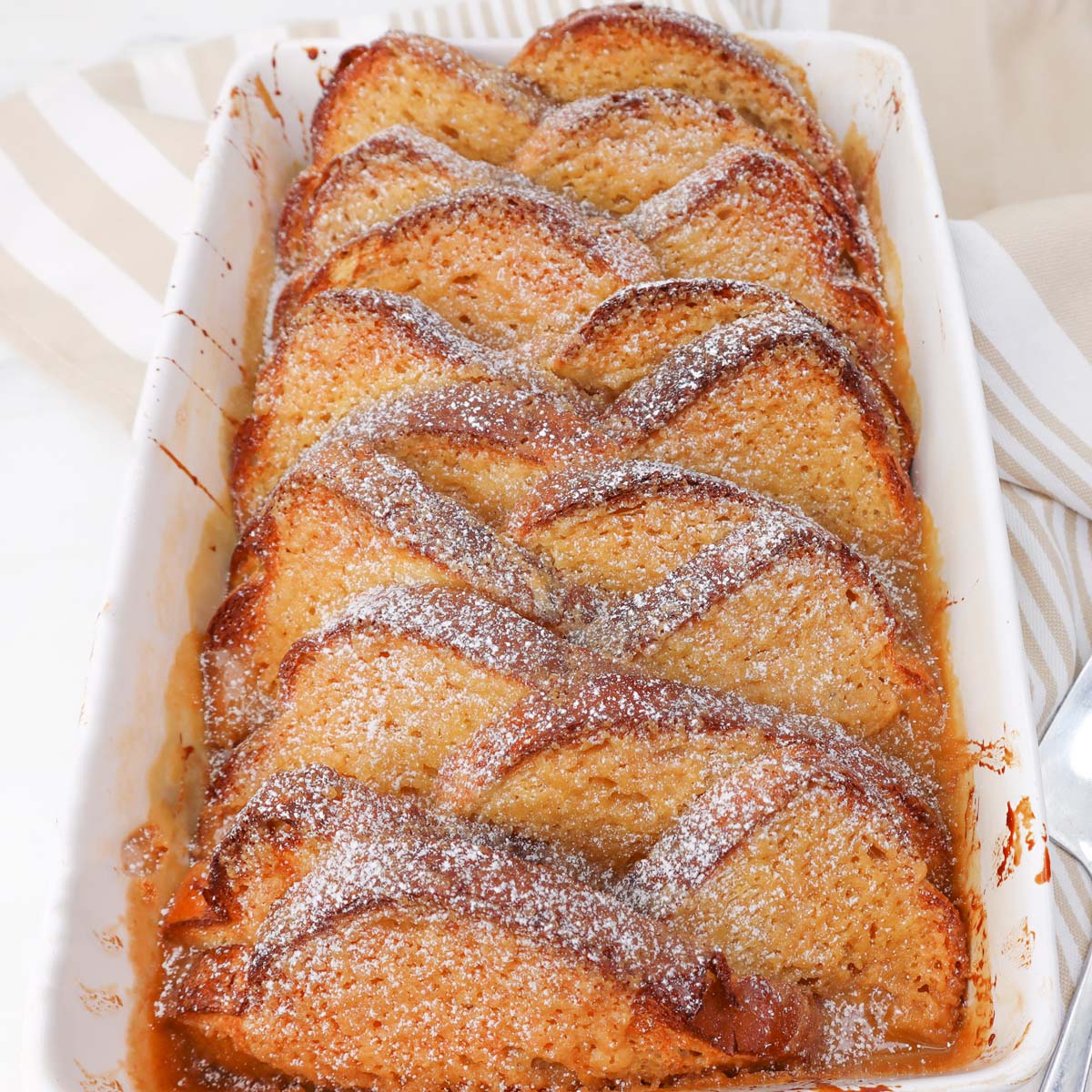 Baked French Toast with Caramel Sauce Baked French toast arranged in a dish, topped with powdered sugar.