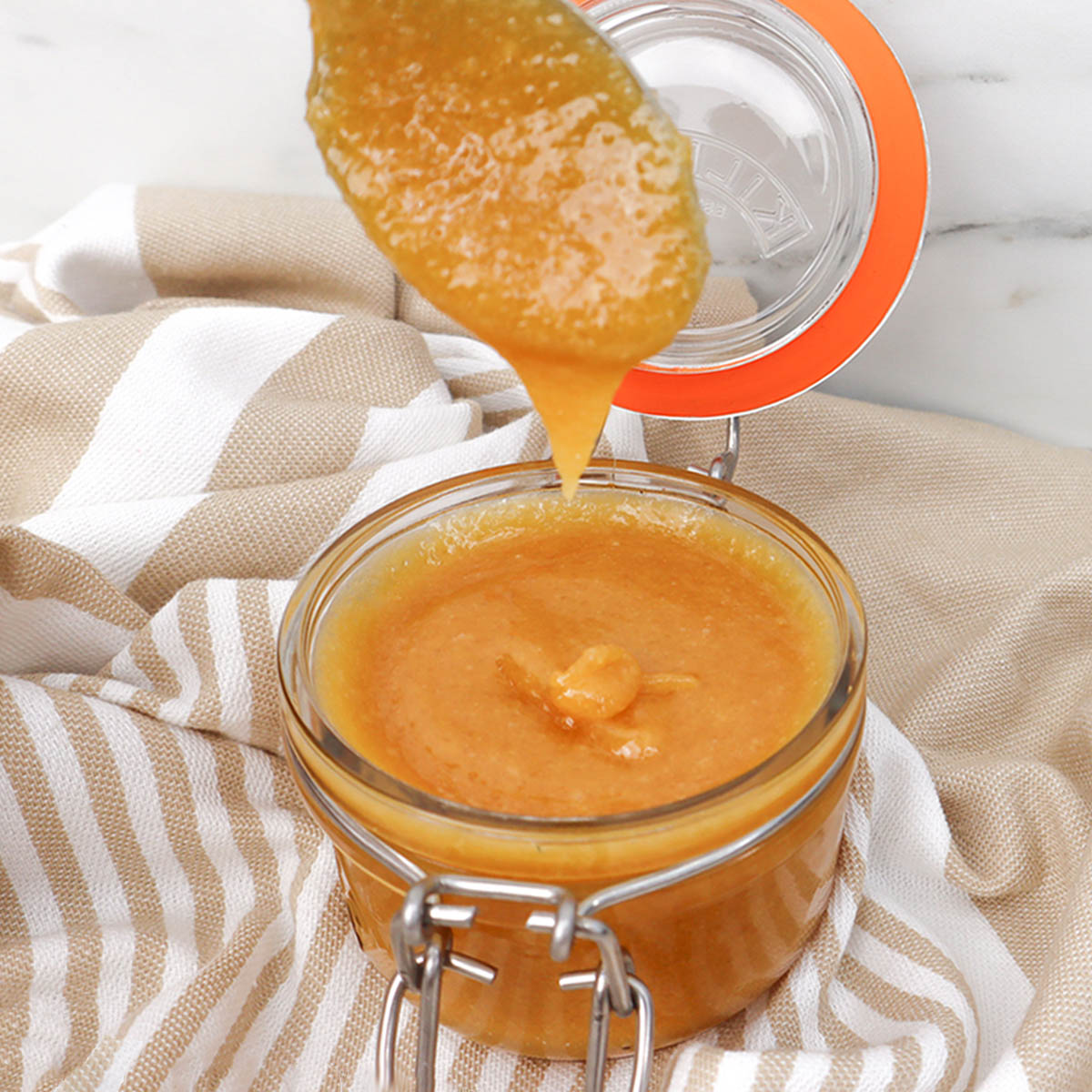 Baked French Toast with Caramel Sauce A spoon drizzling caramel sauce from a glass jar onto a striped cloth.